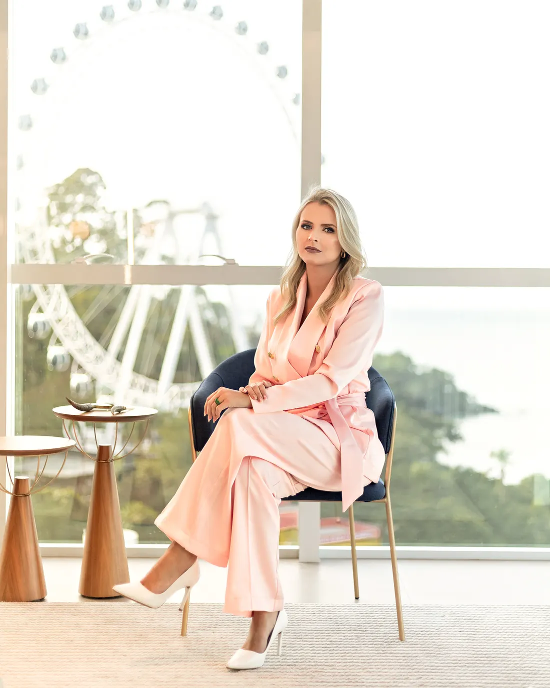 Dra. Ana Winter de terno rosa sentada numa poltrona, com a roda-gigante de Balneário Camboriú ao fundo
